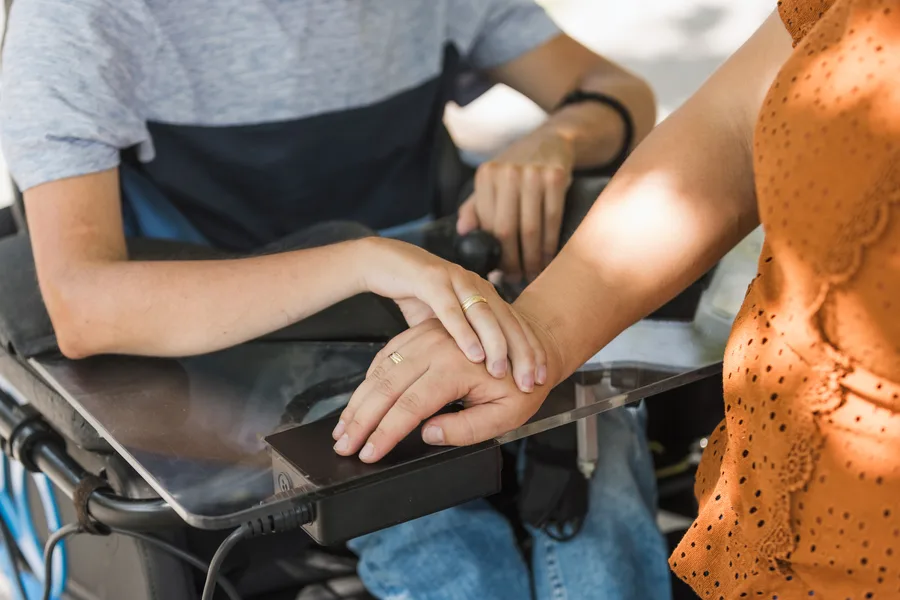 A couple's hands resting gently together — one partner using a powered wheelchair